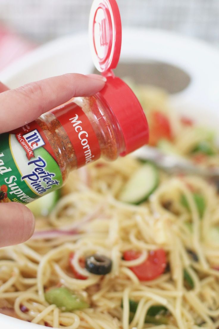 someone is dipping sauce on some noodles in a white bowl with cucumbers and tomatoes