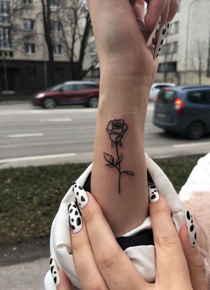 two hands with black and white polka dots holding a rose tattoo on their left wrist