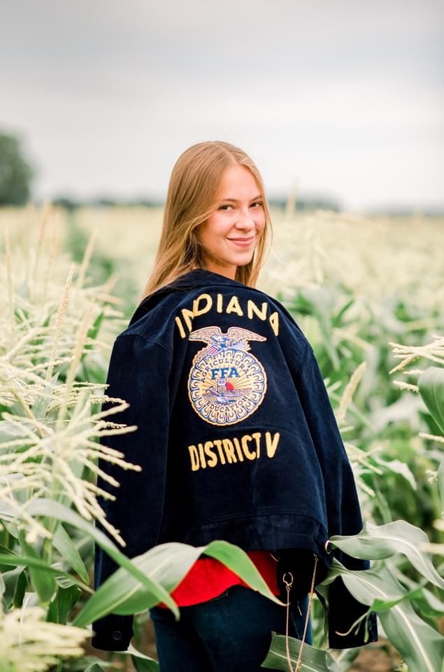 a woman standing in a corn field with a police jacket over her shoulders and the words indiana district written on it