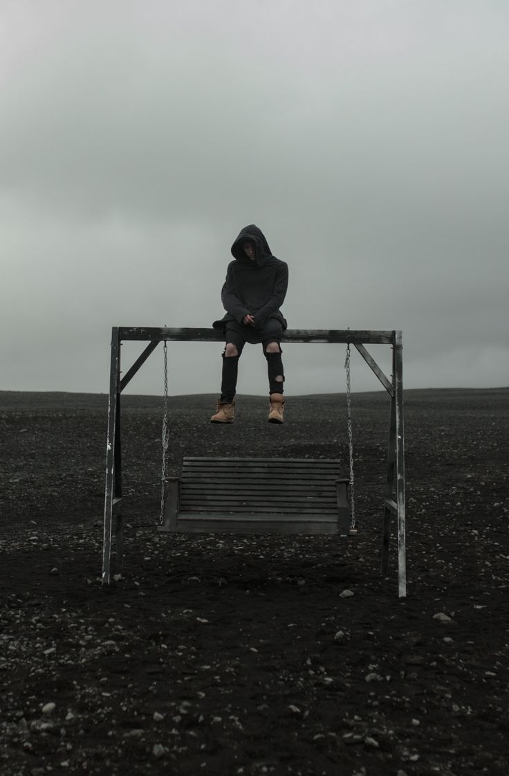 a man sitting on top of a metal bench in the middle of nowhere with his head down