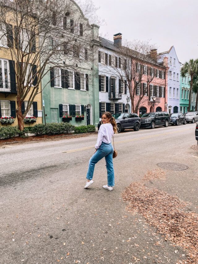 a woman walking down the street in front of parked cars and buildings on both sides