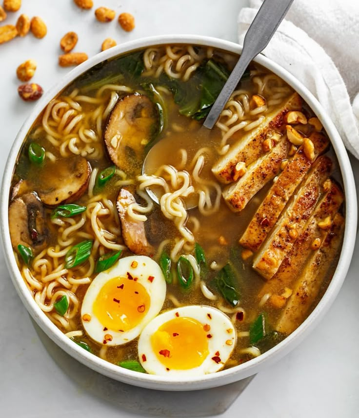 a bowl of ramen with noodles, eggs and spinach in it on a white surface