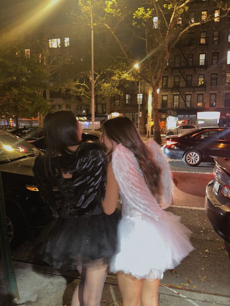 two women in short dresses standing next to each other on the sidewalk at night time