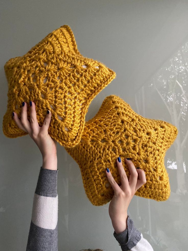 two people holding up yellow crocheted pillows