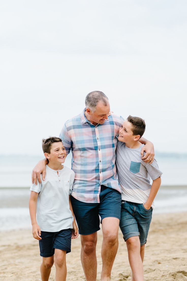 an older man and two young boys walking on the beach with their arms around each other