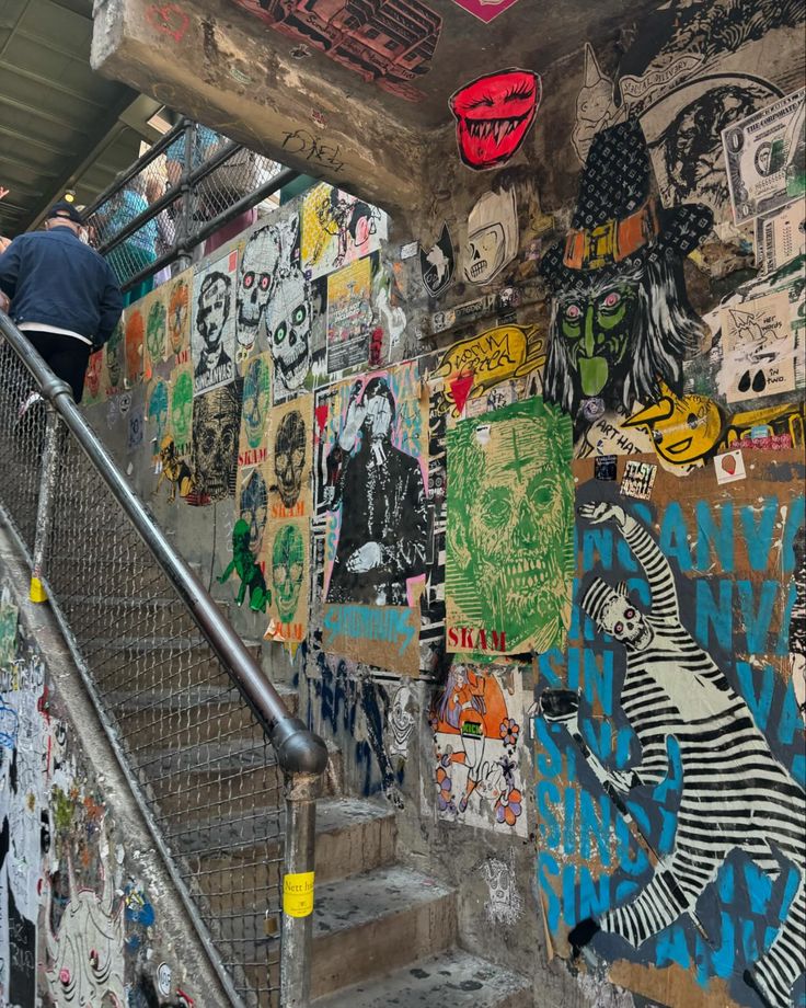 a man climbing up the stairs in front of a wall covered with graffiti and stickers