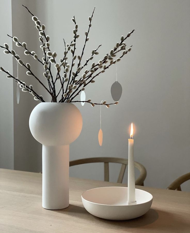 a white vase sitting on top of a wooden table next to a lit candle holder