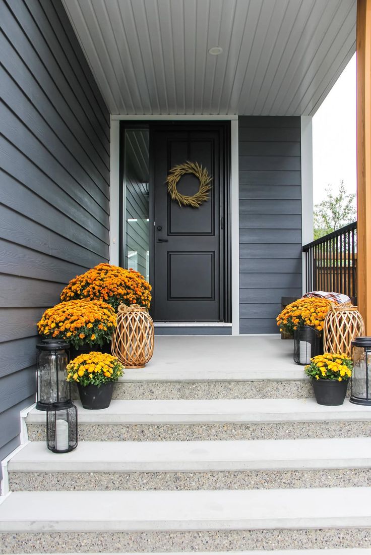 the front porch is decorated with yellow mums and black lanterns for fall decorating