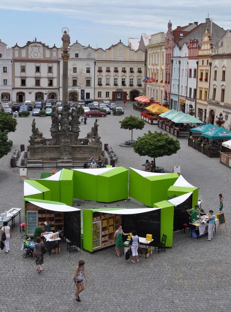 an open air market with people walking around and tables in the foreground, surrounded by buildings