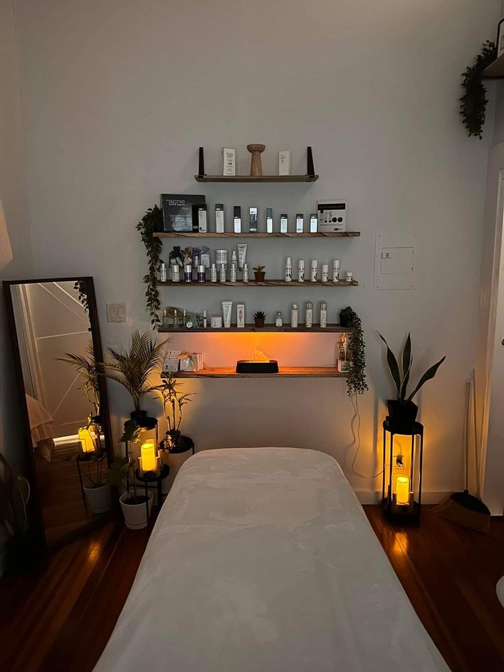 a white bed sitting in a bedroom next to a wall filled with bottles and candles