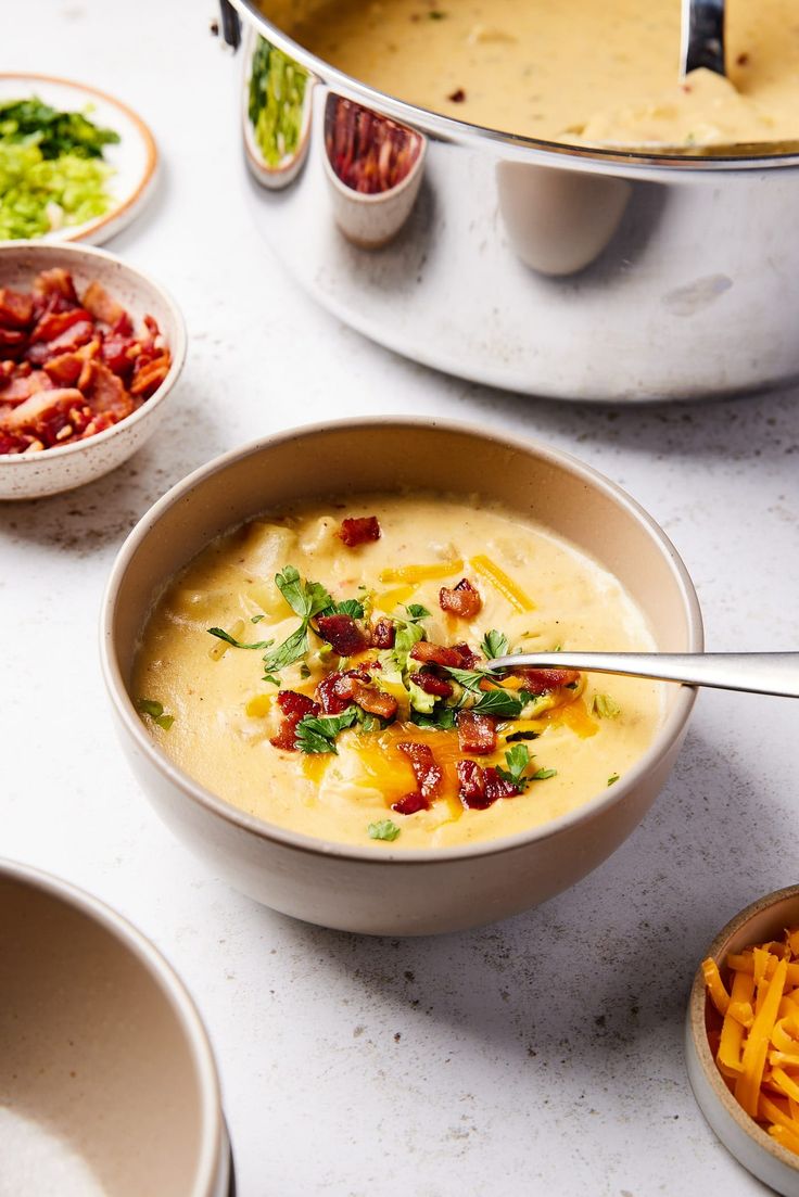 a bowl of soup with cheese and bacon on the side next to other bowls full of food