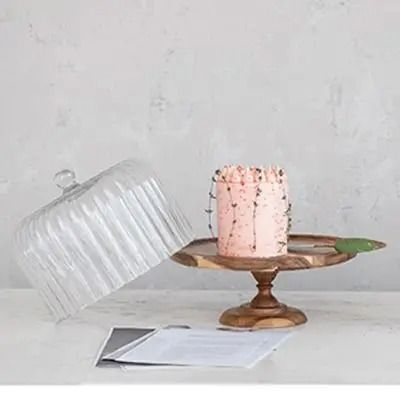 a pink cake sitting on top of a wooden platter next to a plastic container