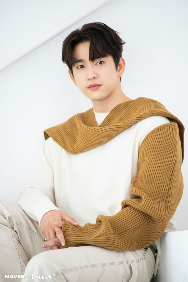 a young man sitting on top of a white chair wearing a brown sweater and khaki pants