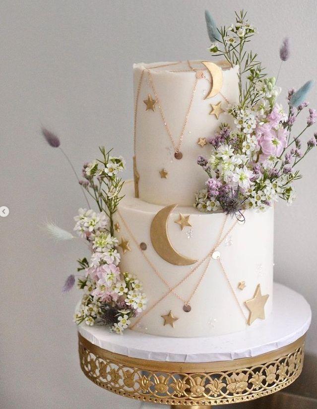 a three tiered white cake decorated with flowers and stars on a gold platter