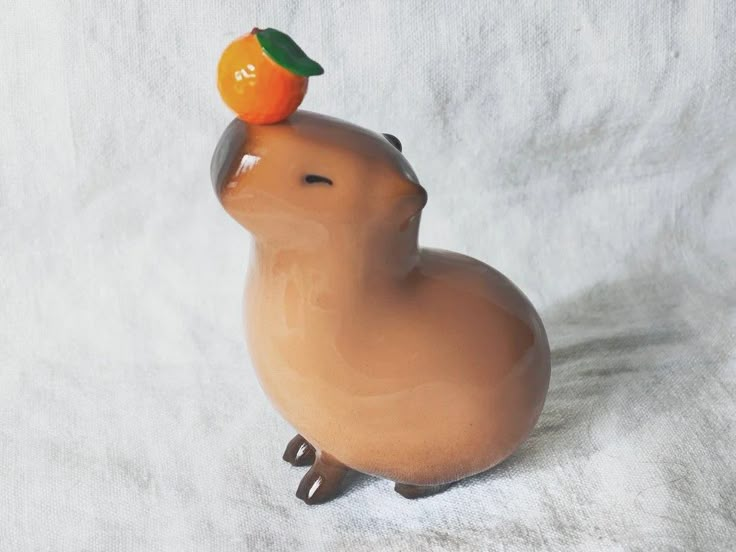 a small ceramic animal with an orange on its head sitting on a white surface,