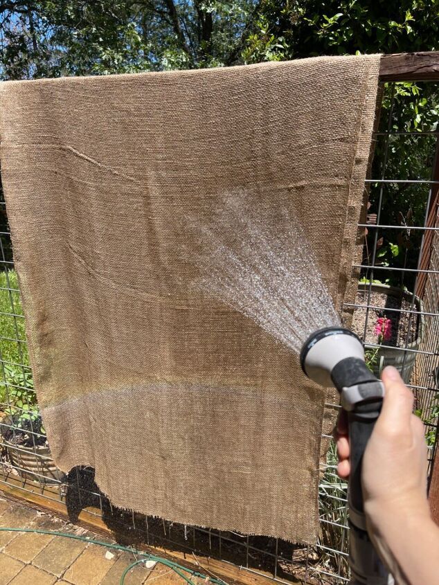 a person spraying water on a piece of cloth in front of a fence with flowers