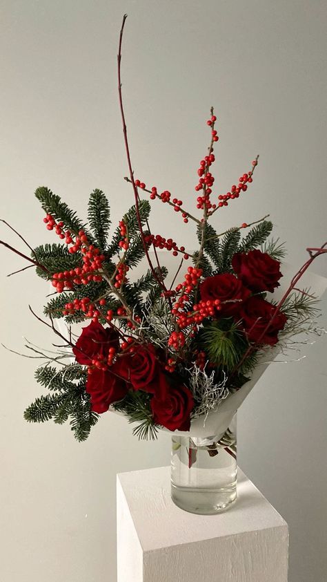 a vase filled with red flowers and greenery sitting on top of a white block