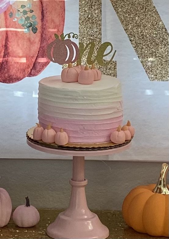 a pink and white cake sitting on top of a table next to small pumpkins