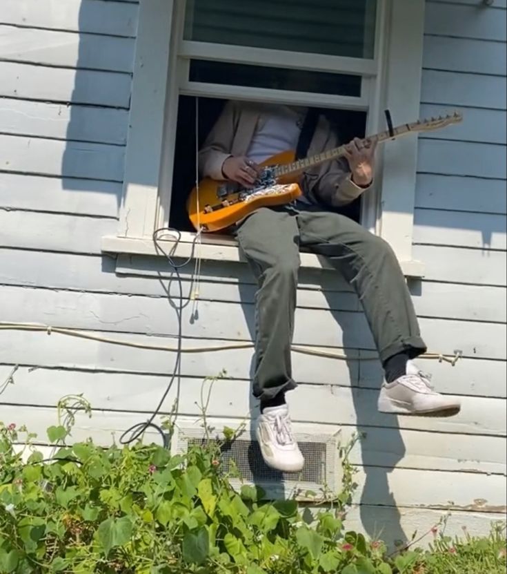 a man sitting on the window sill playing an electric guitar with his feet up