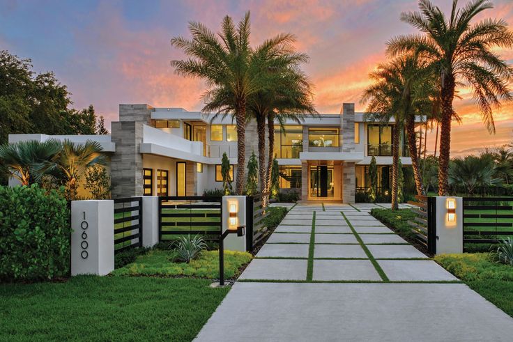 a large house with palm trees in the front yard at sunset or dawn, and an entrance way leading to it