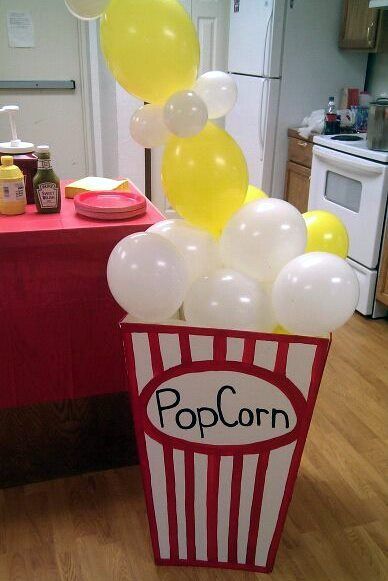 a popcorn box filled with balloons on top of a wooden floor next to a table