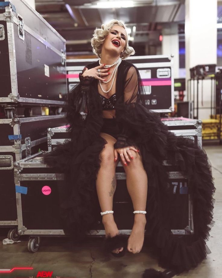 a woman in a black dress sitting on top of a luggage cart with her legs crossed