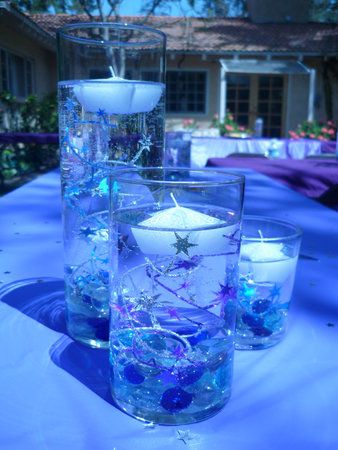 some candles are sitting on a table with blue cloths and glass vases filled with water