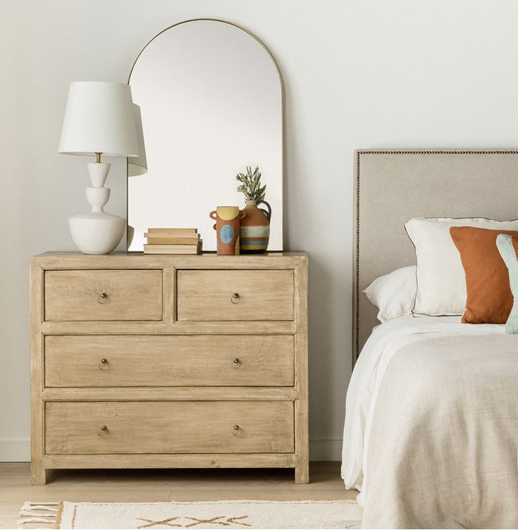 a bedroom scene with focus on the dresser and bed, which has a large mirror above it