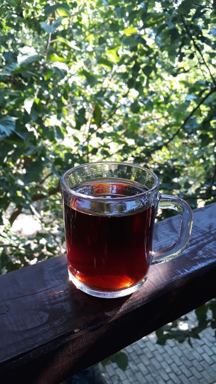 a cup of tea sitting on top of a wooden table next to some leaves and trees