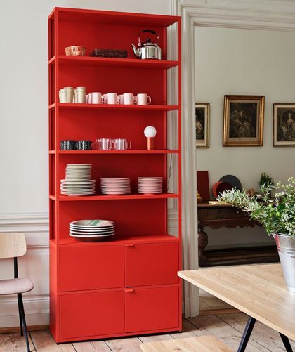 a red bookcase with plates and bowls on it next to a dining room table