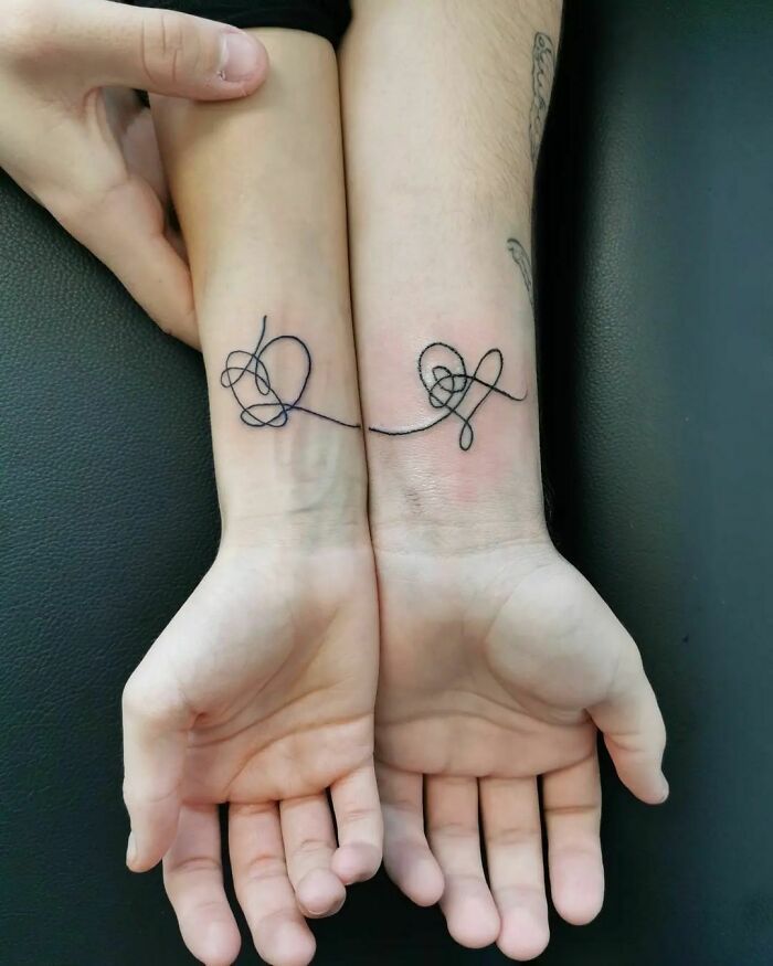 two people with matching tattoos on their arms, one holding the other's hand