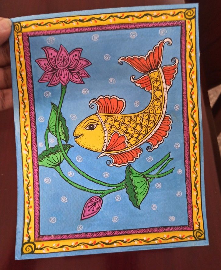 a person holding up a painting with a gold fish on it's face and flowers in the background