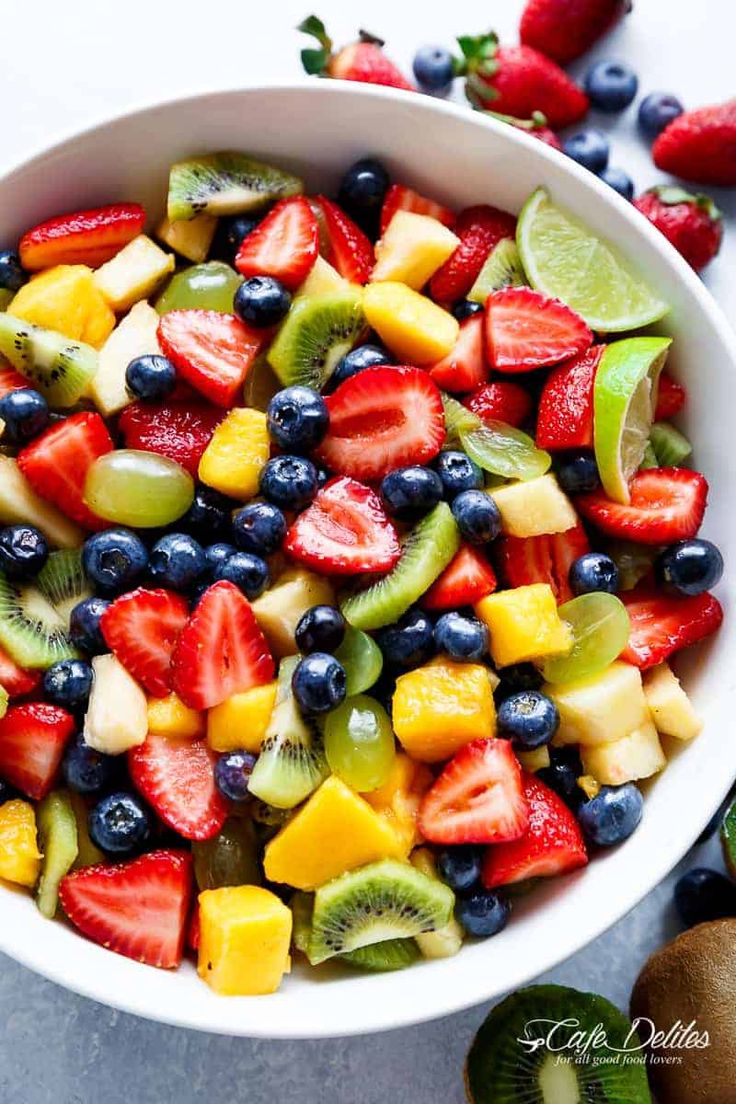 a fruit salad with kiwi, blueberries, strawberries and oranges in a white bowl