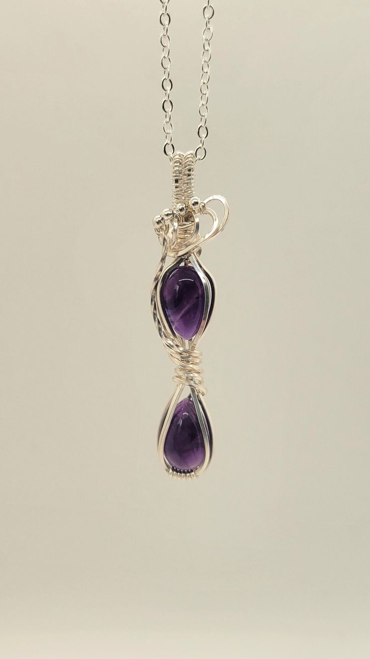 Two beautifully pear cut Amethyst cabochons set in this Hourglass necklace wrapped with silver plated tarnish resistant artist wire and silver filled artist wire. It has been accented with twisted artist wire and silver beads.  It measures approximately .25" inches in width by 2" in length.  It is a very dainty piece that will make a great addition to any gemstone jewelry collection.  Amethyst is believed to carry the energy of fire and passion, creativity and spirituality.  To the ancients it w Silver Wire Necklaces As A Gift, Silver Wire Necklaces Gift, Silver Wire Necklace Gift, Silver Wire Wrapped Necklace, Silver Wire-wrapped Necklace, Silver Hand Wrapped Metal Necklace, Unique Silver Wire Necklaces, Silver Teardrop Wire Wrapped Necklaces, Silver Teardrop Wire Wrapped Necklace