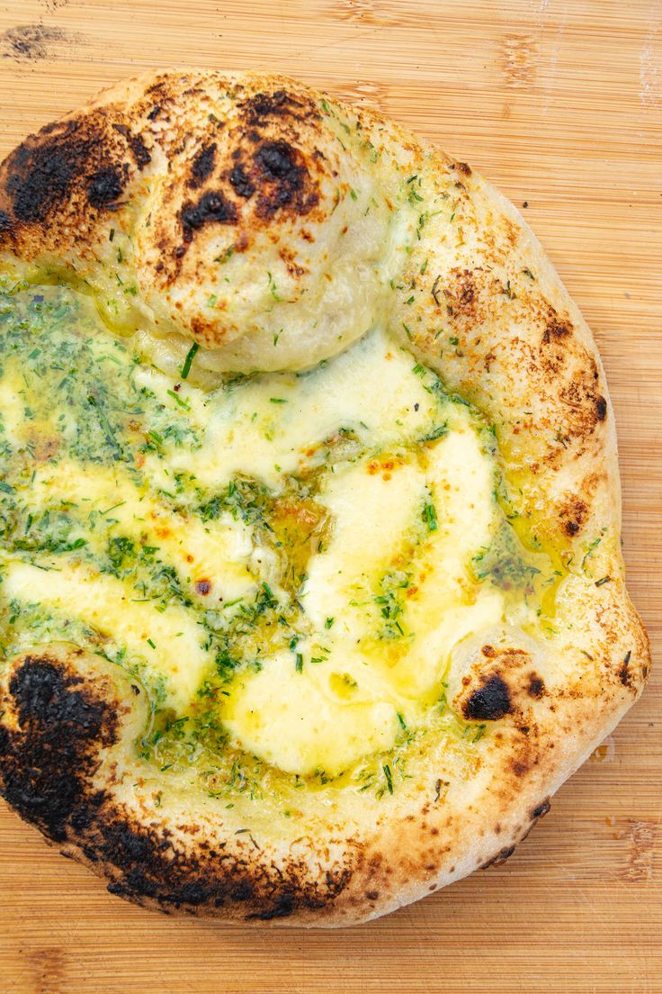 a pizza sitting on top of a wooden cutting board covered in cheese and pesto