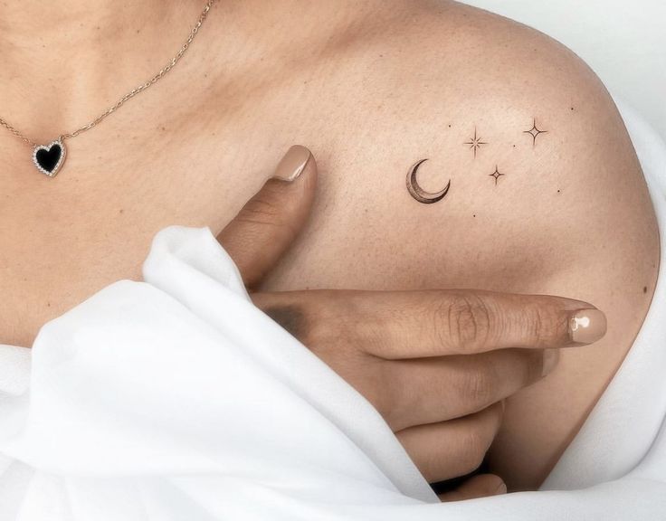 a woman with her hand on her chest holding the moon and star tattoo above her left shoulder