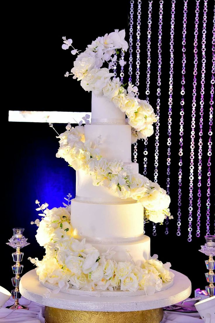 a wedding cake with white flowers on top is surrounded by candles and beaded garlands