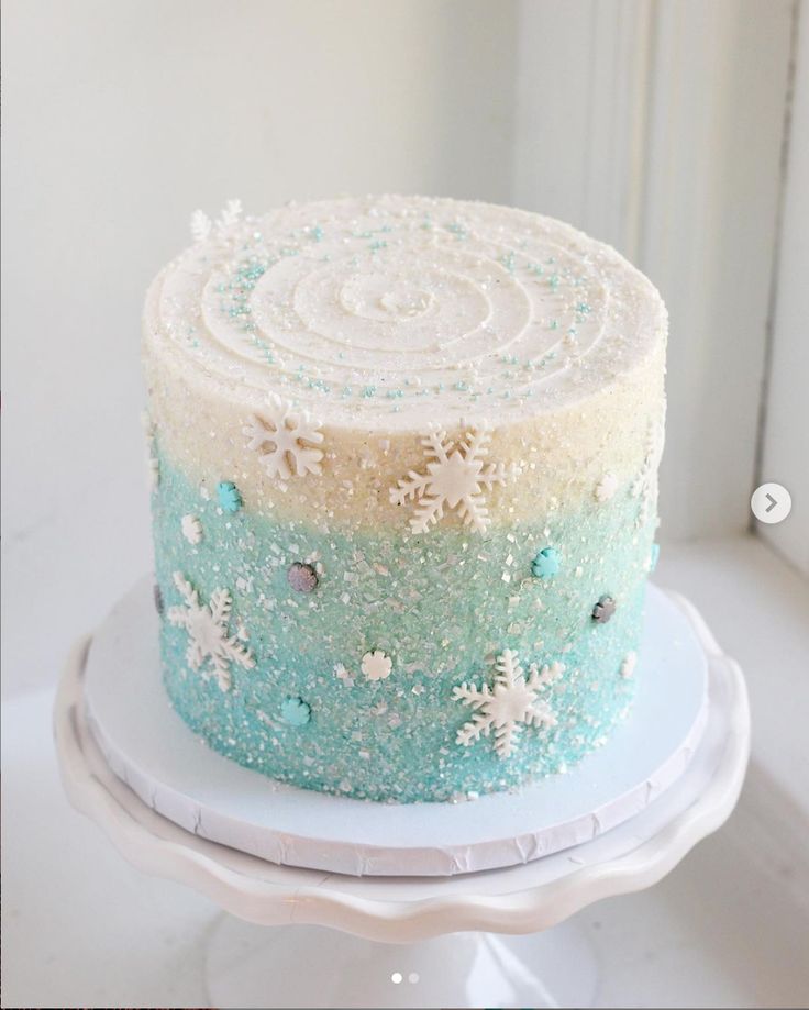 a frosted cake sitting on top of a white plate covered in snowflakes