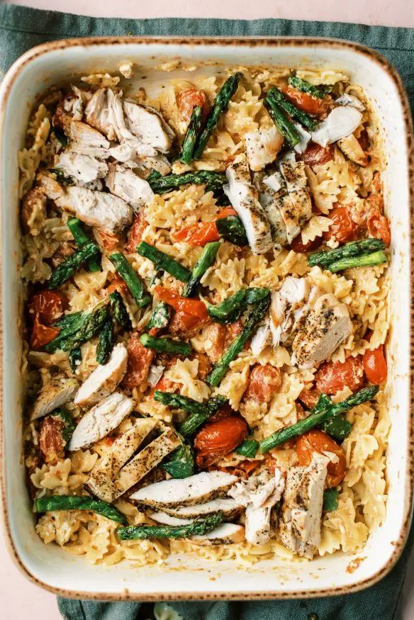 an image of pasta with chicken and tomatoes in a white casserole dish on a table