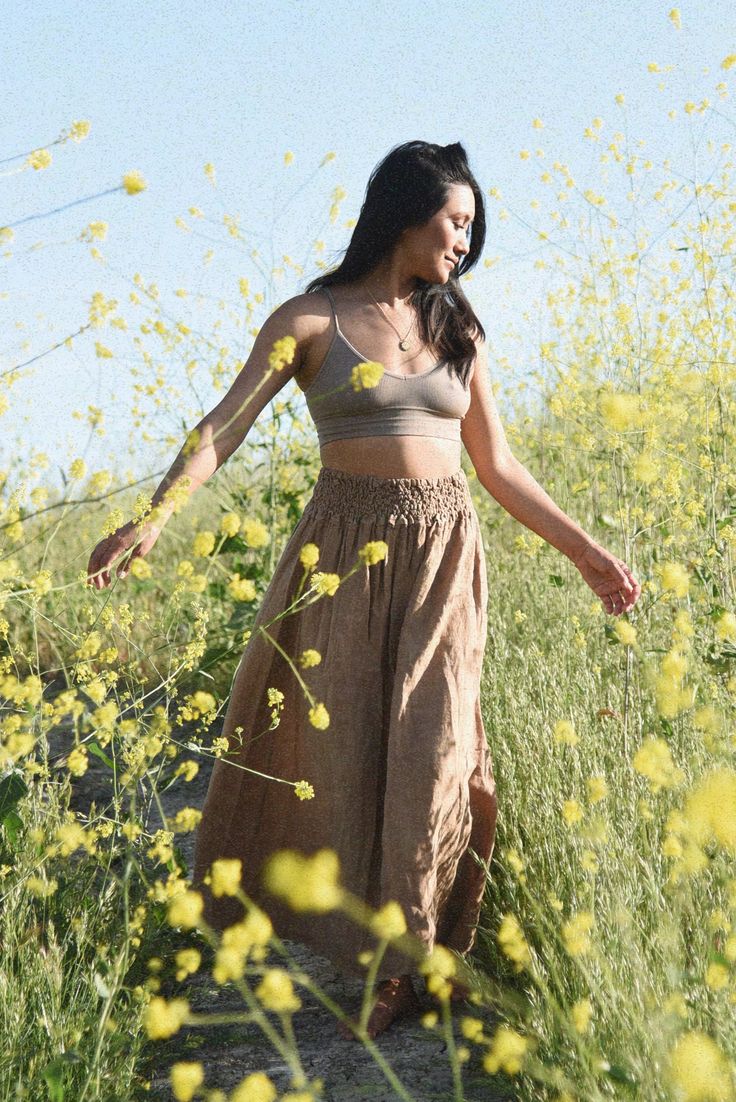 a woman in a long skirt walking through a field with yellow flowers on the ground