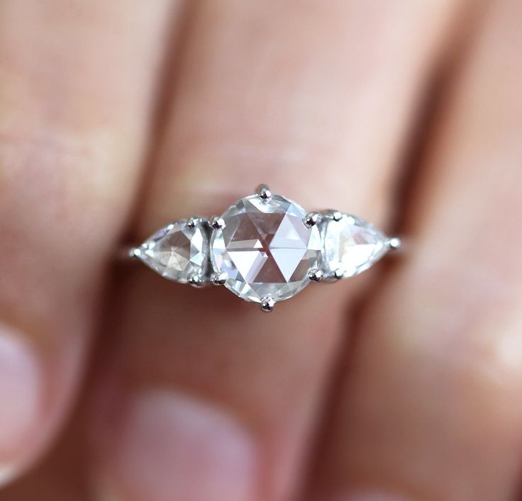 a woman's hand holding an engagement ring with three pear shaped diamonds on it