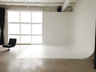 an empty room with white walls and black chair in the middle, next to a large window