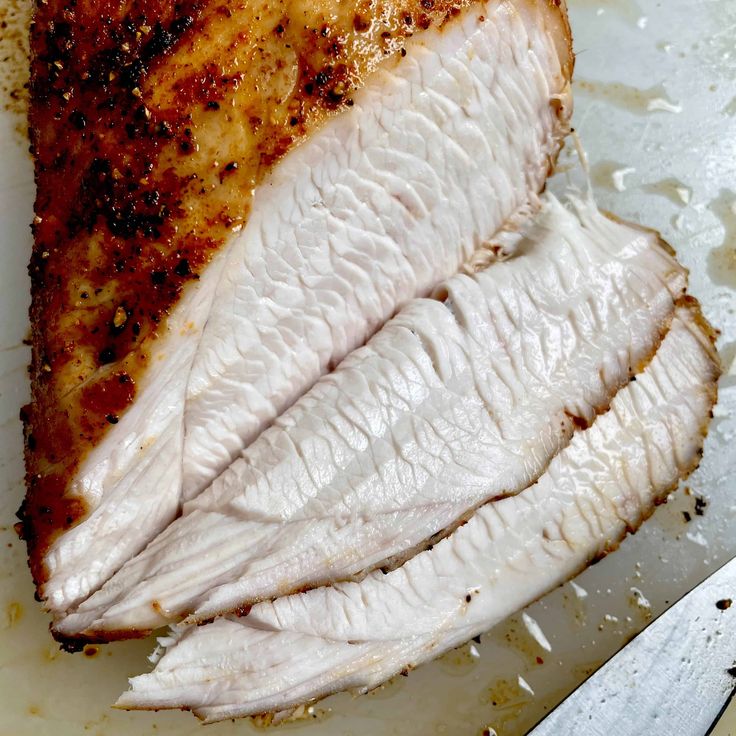 a piece of chicken sitting on top of a white cutting board next to a knife