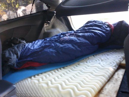 a man sleeping in the back seat of a car with his feet on an air mattress