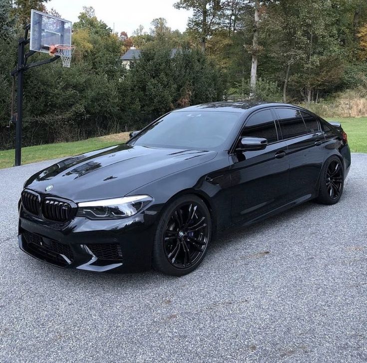 a black car parked on the side of a road next to a basketball hoop with trees in the background