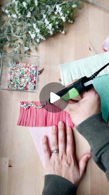 someone is making something out of paper on the table with flowers and scissors in front of them