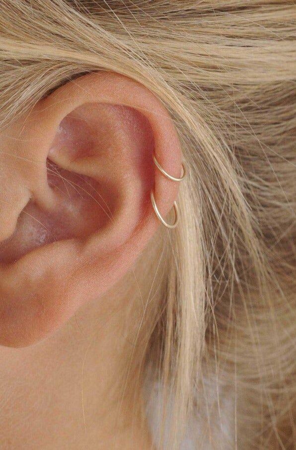 a woman's ear is shown with two thin gold hoops