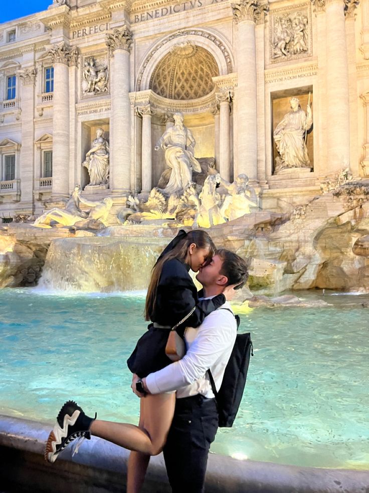 a man and woman kissing in front of a fountain