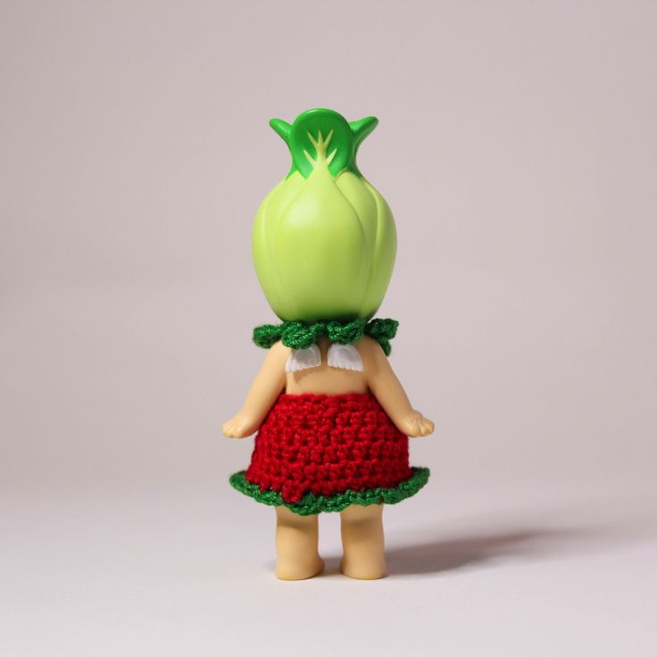 a small doll with a green head and red dress is standing in front of a white background