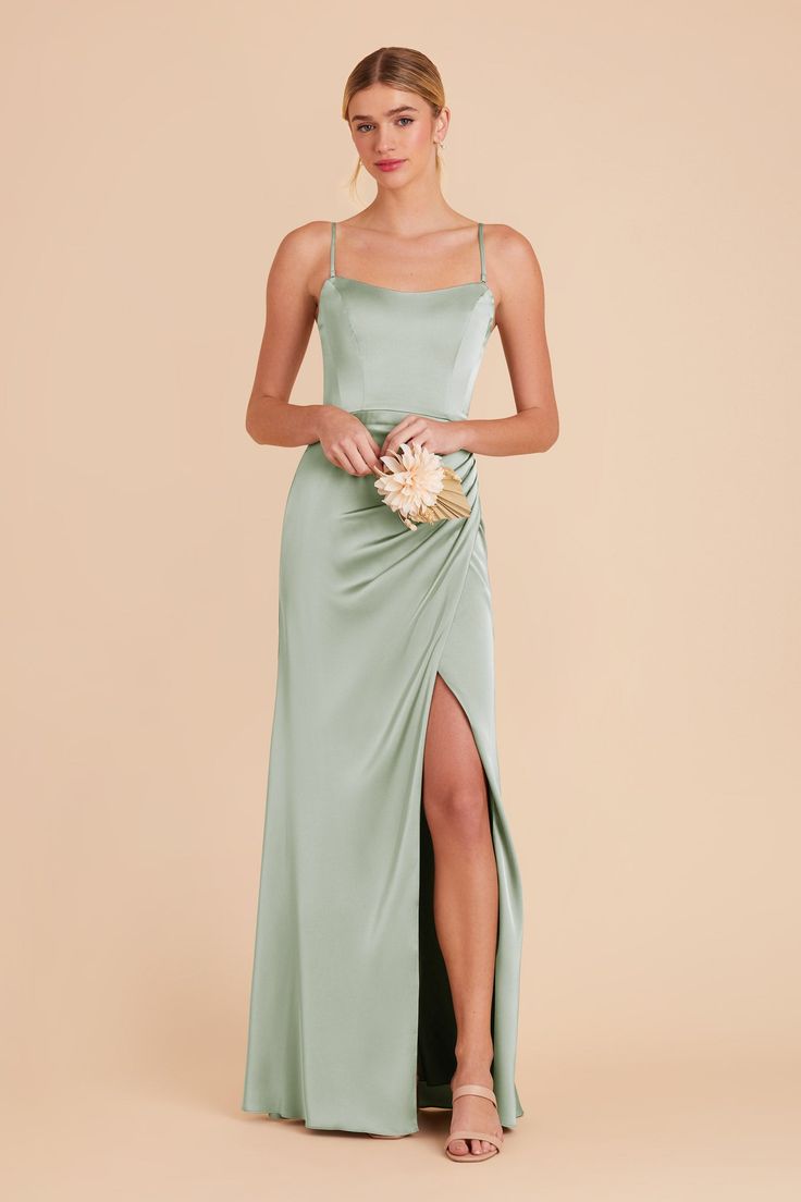 a woman in a long green dress is holding a flower and posing for the camera